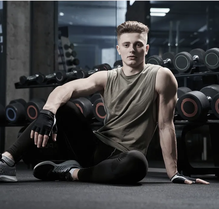 Young man resting on gym floor beside dumbbells.
